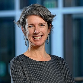 Alison Brown smiles at the camera in front of a blue and green interior background. 